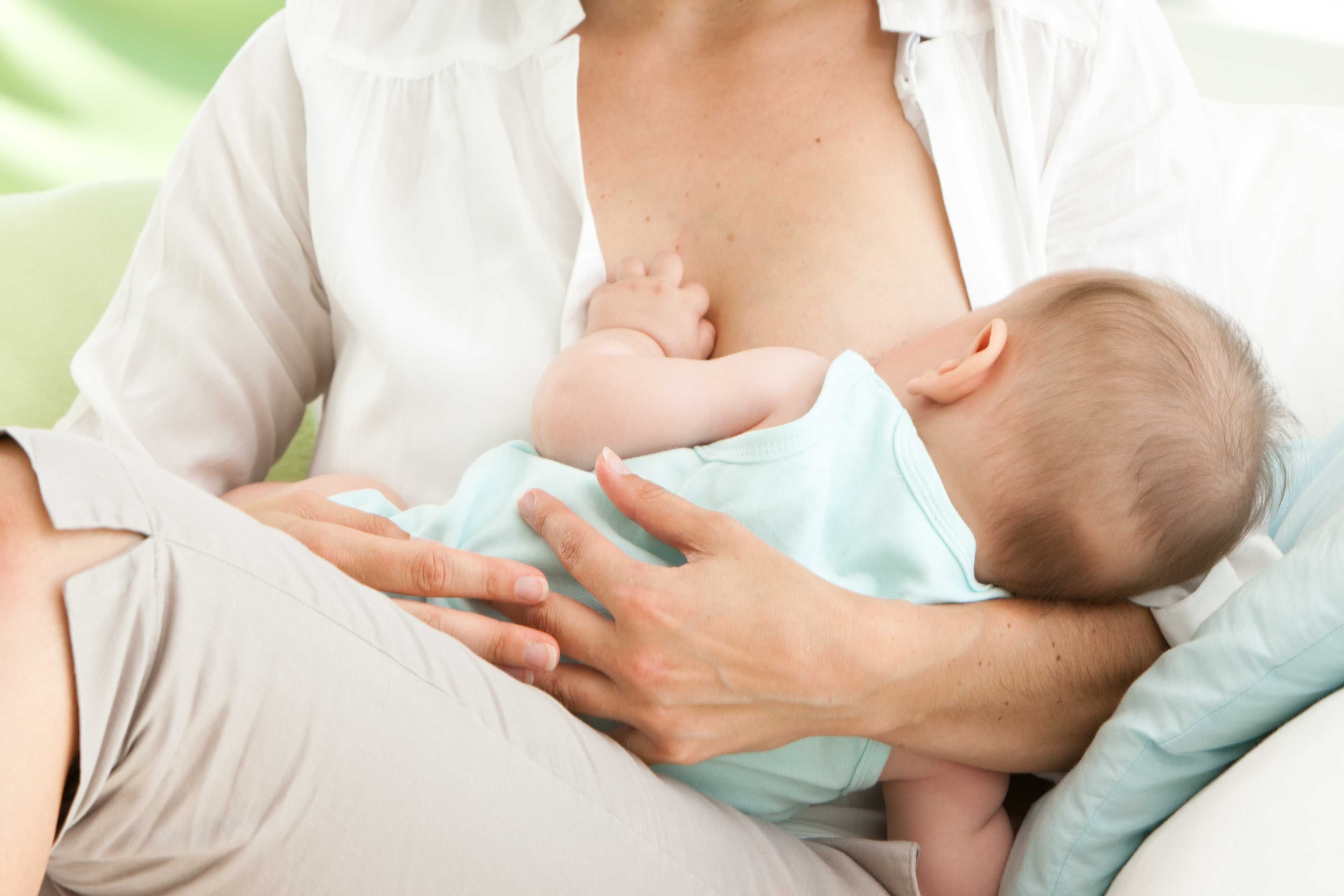 Eine Frau, die ihr Baby bequem stillt, mit einem weichen Fokus auf den Kopf des Babys und die Brust der Frau.