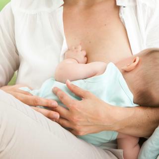 Eine Frau, die ihr Baby bequem stillt, mit einem weichen Fokus auf den Kopf des Babys und die Brust der Frau.
