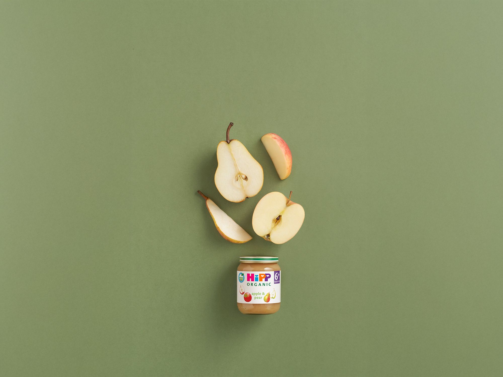 HiPP Organic Apple & Pear baby food jar with fresh apple and pear slices on a soft green background