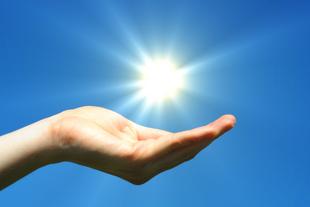 Geöffnete Hand unter strahlender Sonne vor blauem Himmel als Symbol für Vitamin D, das Sonnenvitamin für starke Knochen