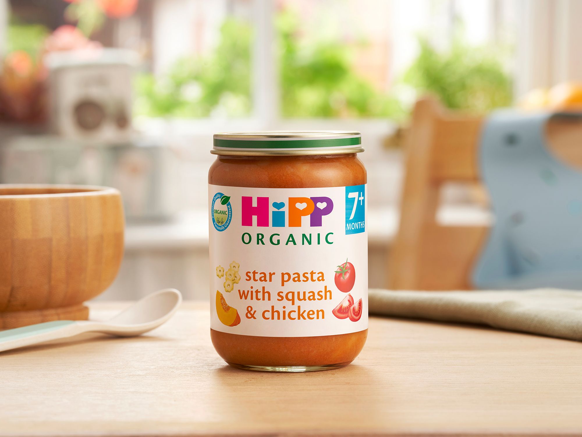 HiPP Organic Star pasta with Squash & Chicken on a dining table next to a bowl and spoon