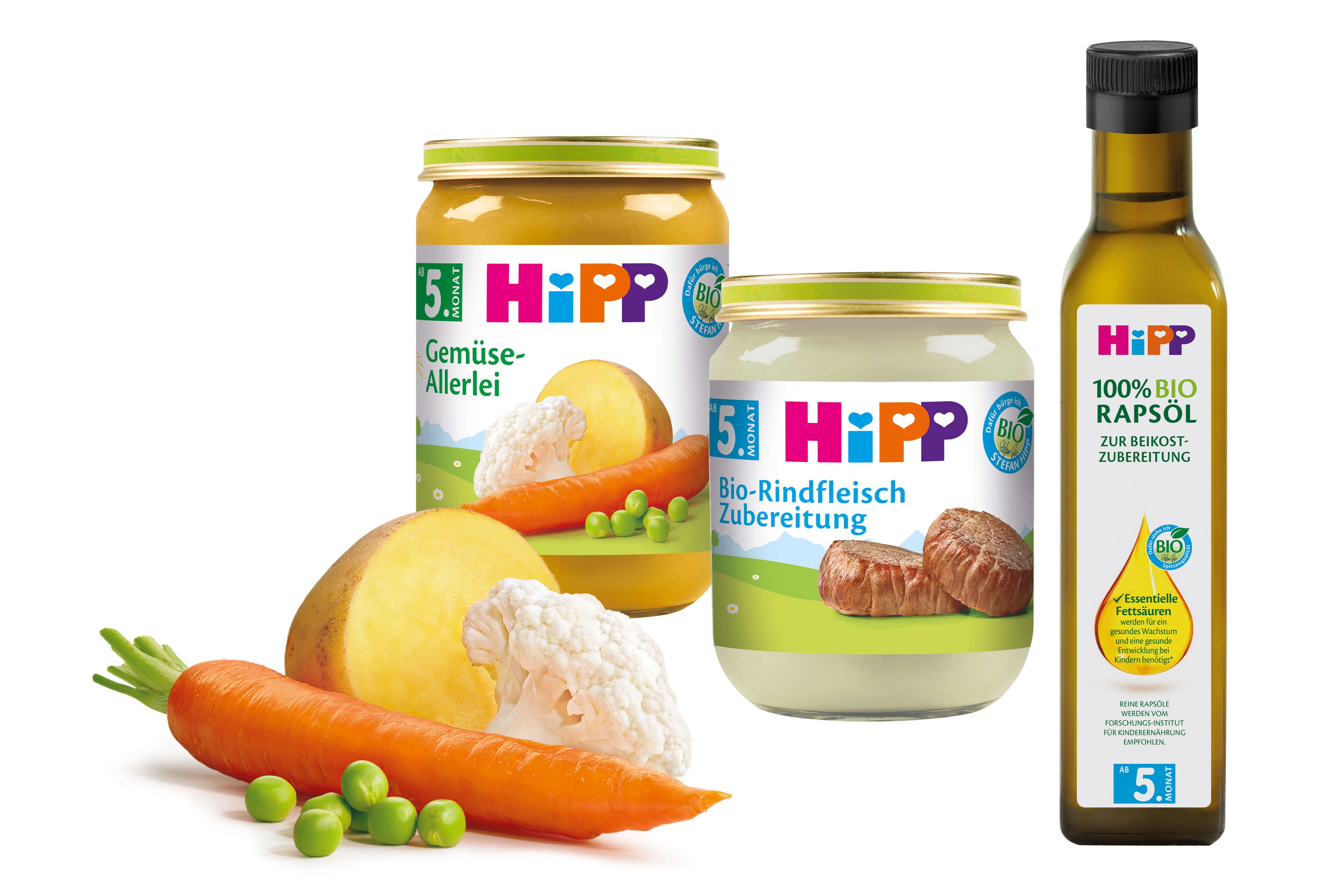 Eine Reihe von Babynahrungsprodukten der Marke "Hipp", darunter Gläser mit Karotten- und Orangenpüree und eine Flasche Olivenöl.