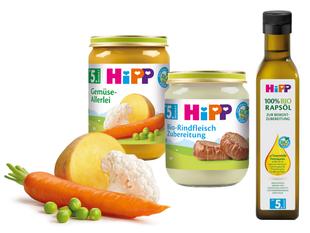 Eine Reihe von Babynahrungsprodukten der Marke "Hipp", darunter Gläser mit Karotten- und Orangenpüree und eine Flasche Olivenöl.