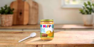 HiPP Bio-Gläschen Kürbis mit Kartoffeln & Bio-Rind ab dem 5. Monat auf Holztisch mit Löffel in heller Küche