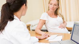 Eine ärztliche Konsultation zwischen einer Ärztin und einer schwangeren Patientin, wobei die Ärztin ein Klemmbrett in der Hand hält und die Patientin über ihre gesundheitlichen Probleme spricht.