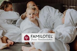 Mutter entspannt mit Baby und zwei Kindern in weißen Bademänteln im Familotel.