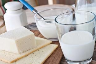 Verschiedene Molkereiprodukte, darunter ein Stück Käse, ein Glas Milch und ein Behälter mit Joghurt, die alle auf einer Holzunterlage platziert sind.