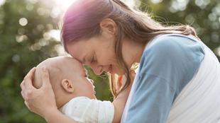 Frau hält ein Baby im Arm und berührt sanft dessen Kopf im Freien