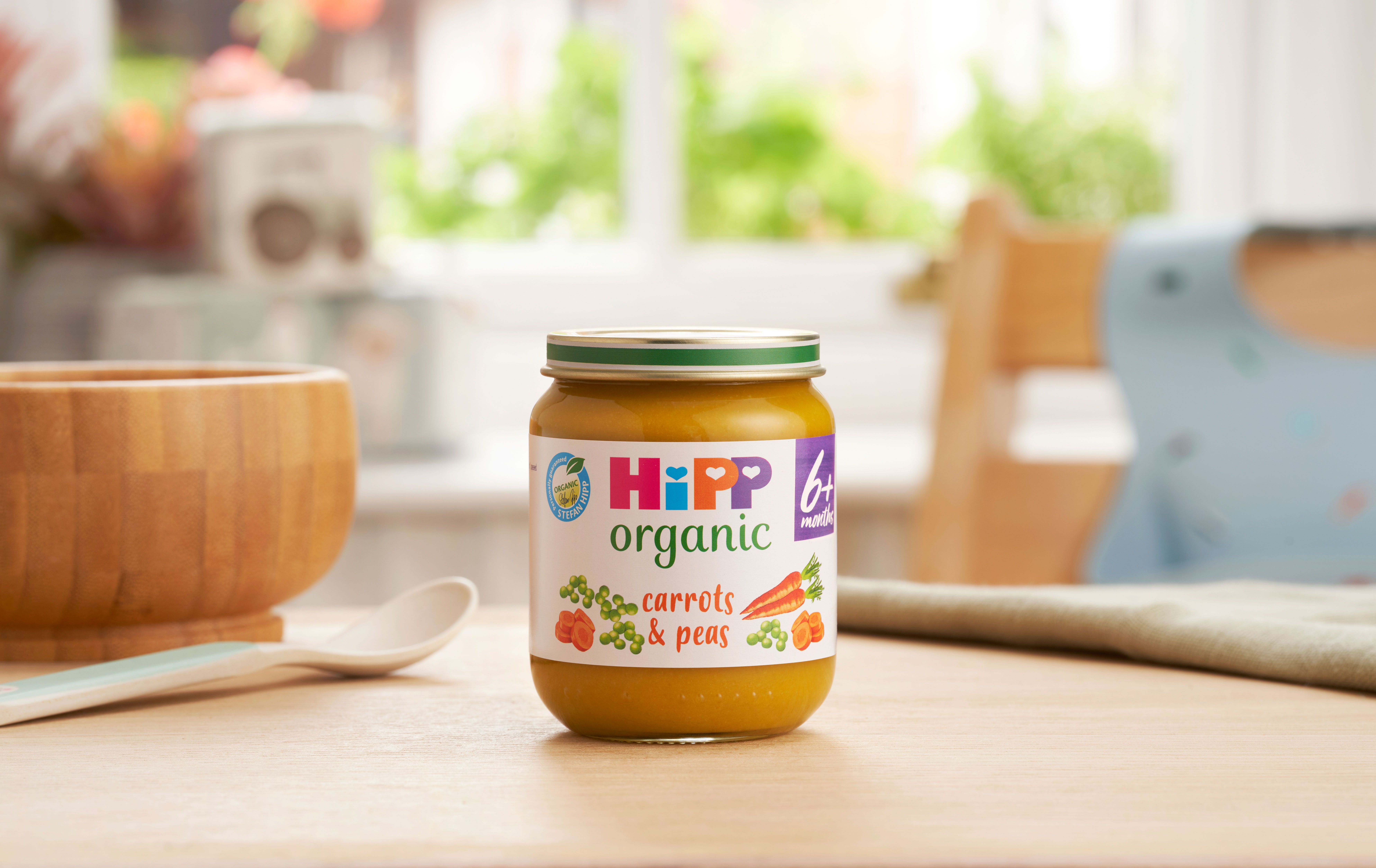 HiPP Organic Carrots & Peas on a dining table next to a bowl and spoon
