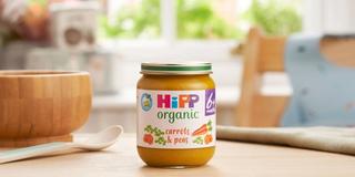 HiPP Organic Carrots & Peas on a dining table next to a bowl and spoon
