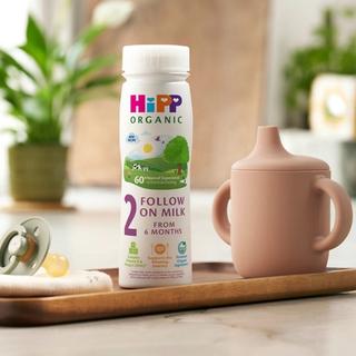 HiPP Organic follow on milk ready to feed bottle on a tray beside a pastel sippy cup and dummy on a bright kitchen worktop