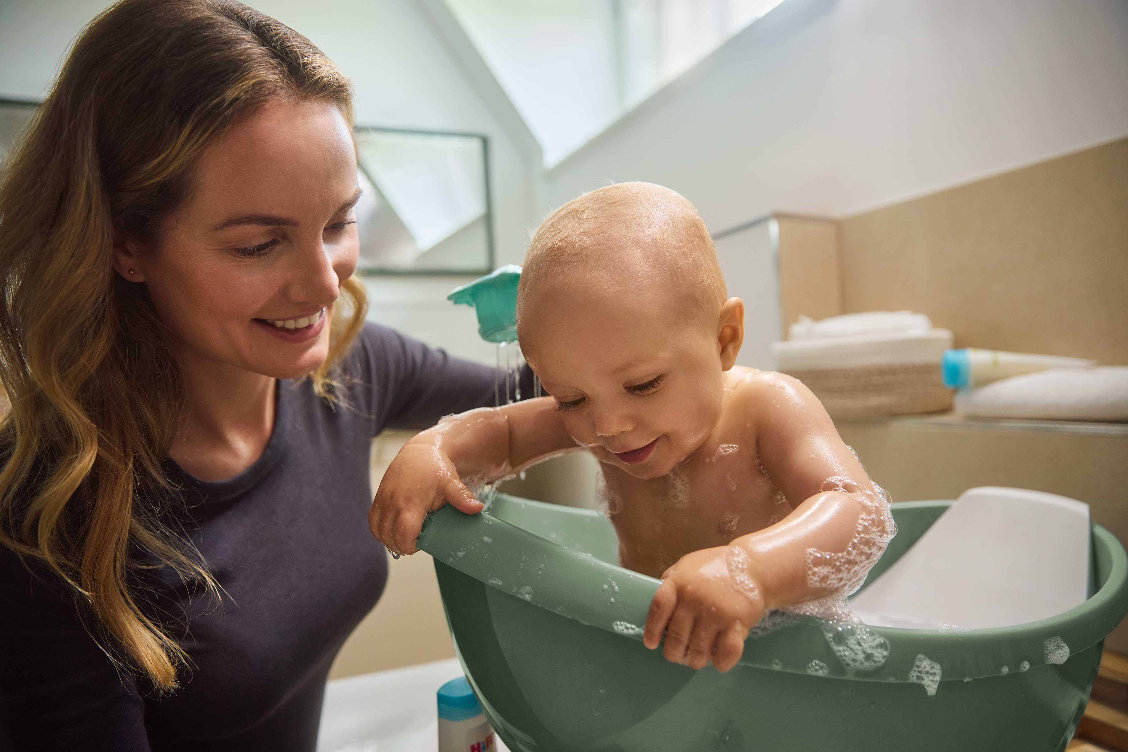 Lächelnde Mutter badet ihr Baby mit mildem Babyshampoo und Waschgel.