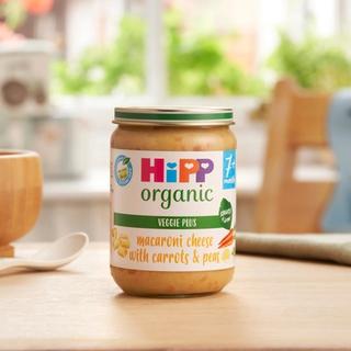 HiPP Organic Macaroni Cheese With Carrots & Peas on a dining table next to a bowl and spoon