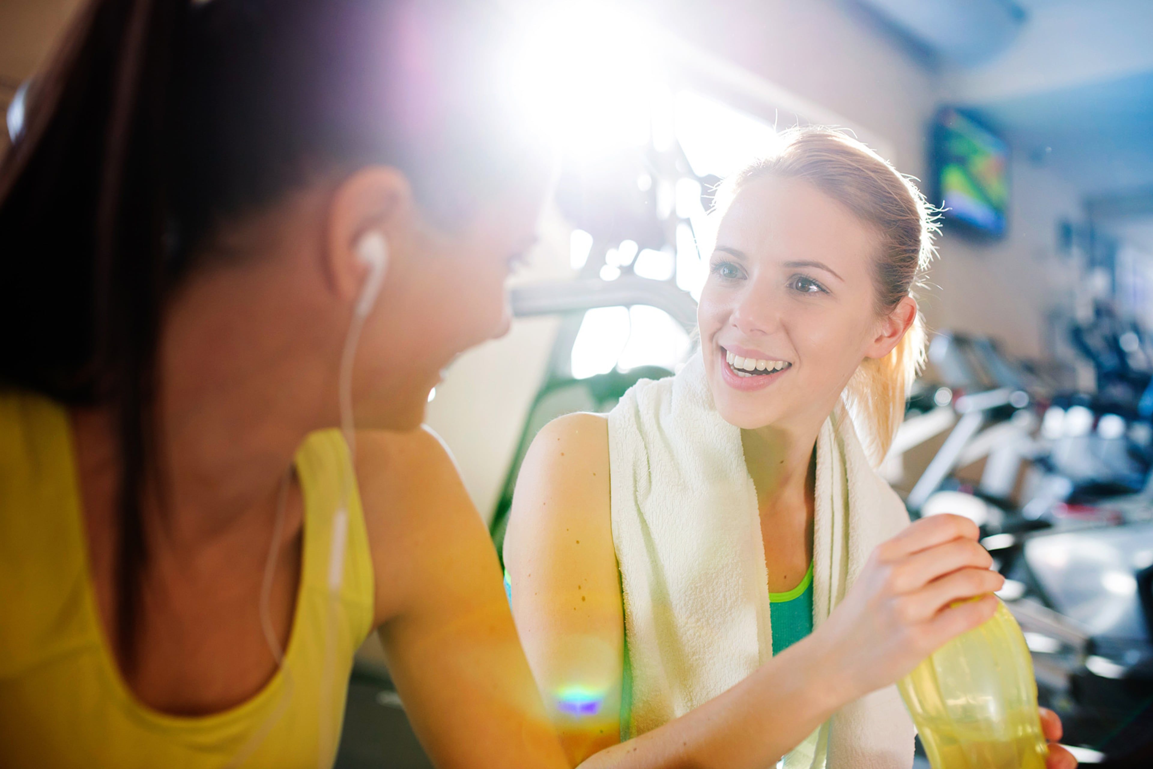Zwei Frauen in einem Fitnessstudio, eine trägt Kopfhörer, die andere lächelt.