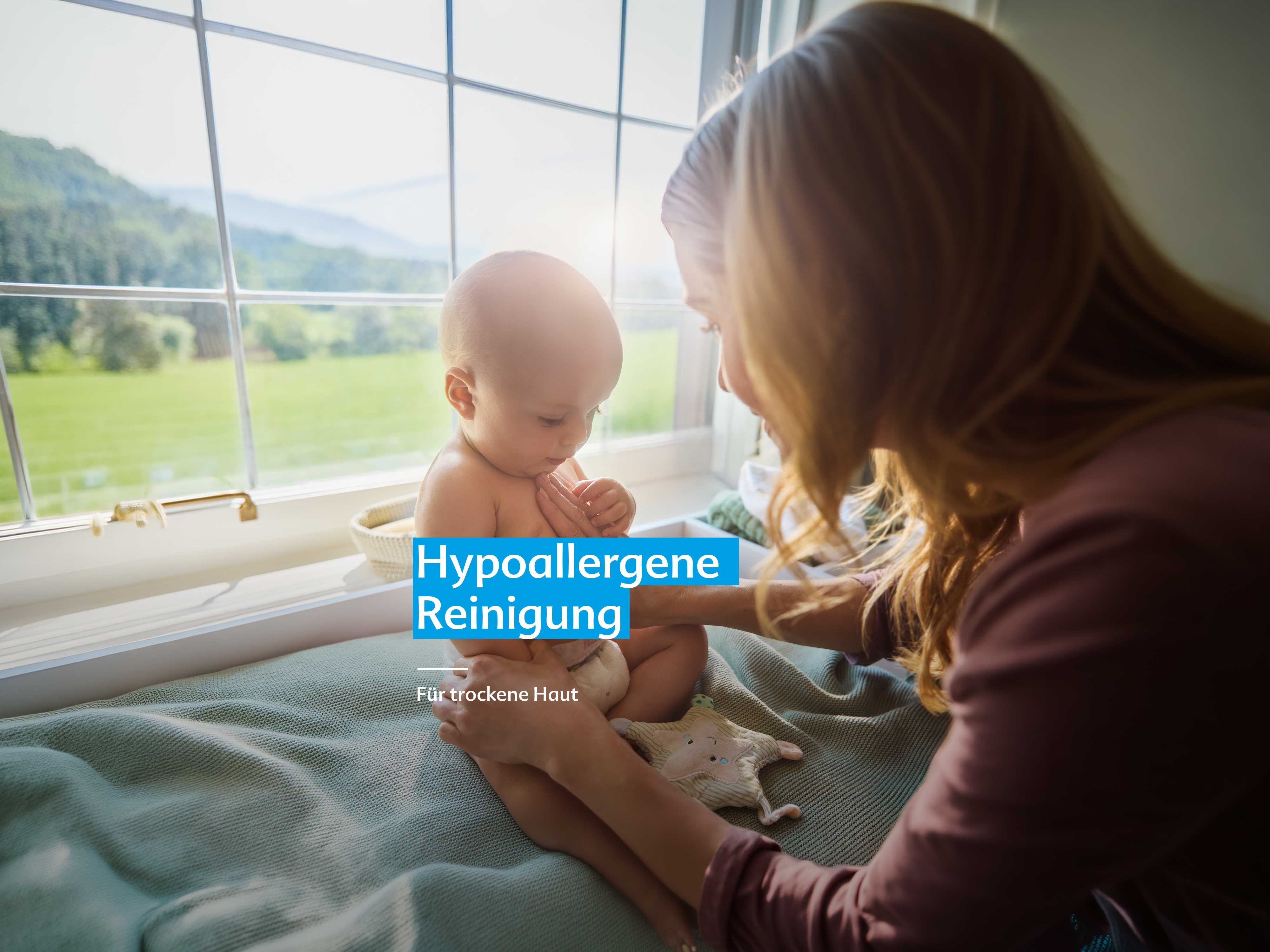 Mutter hält Baby sitzend auf einer Fensterbank mit grüner Landschaft im Hintergrund