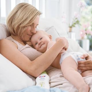 Ein zärtlicher Moment zwischen einer Frau und einem Baby, wobei die Frau das Baby sanft an ihr Gesicht drückt.