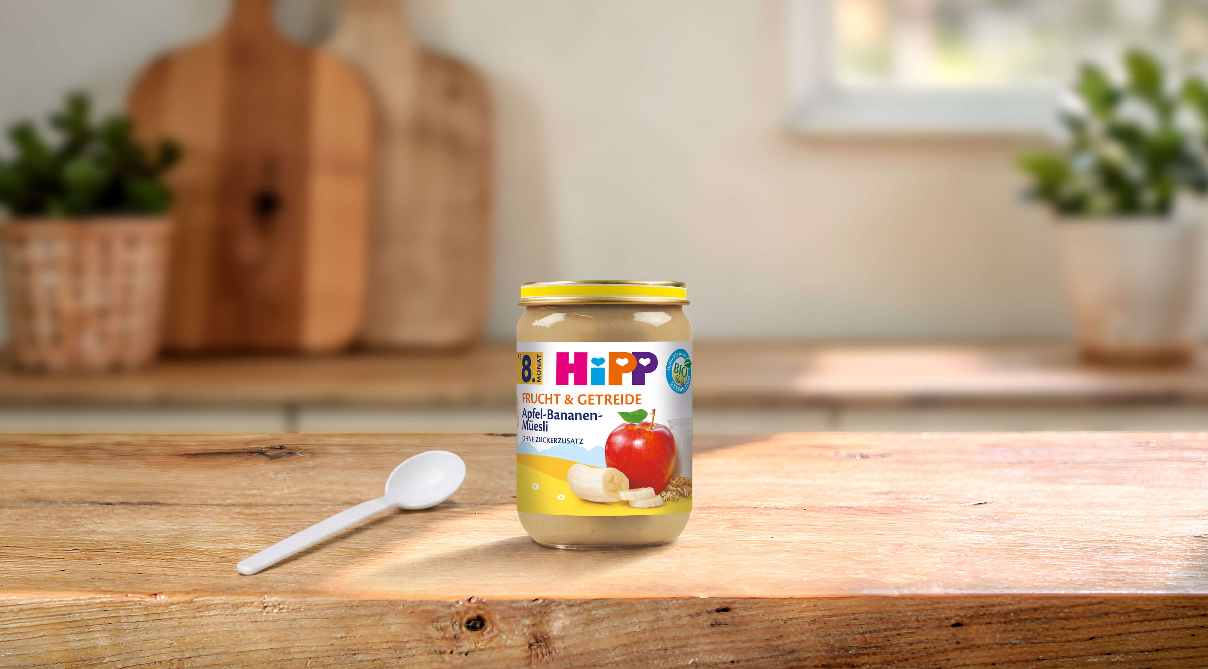 HiPP Bio Frucht & Getreide Apfel-Bananen-Müesli Glas ab 8. Monat auf Holztisch mit Löffel in heller Küche