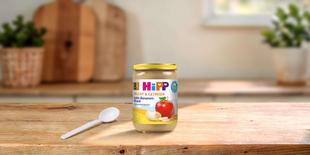 HiPP Bio Frucht & Getreide Apfel-Bananen-Müesli Glas ab 8. Monat auf Holztisch mit Löffel in heller Küche