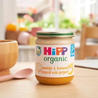 HiPP Organic Mango & Banana topped with Yogurt on a dining table next to a bowl and spoon