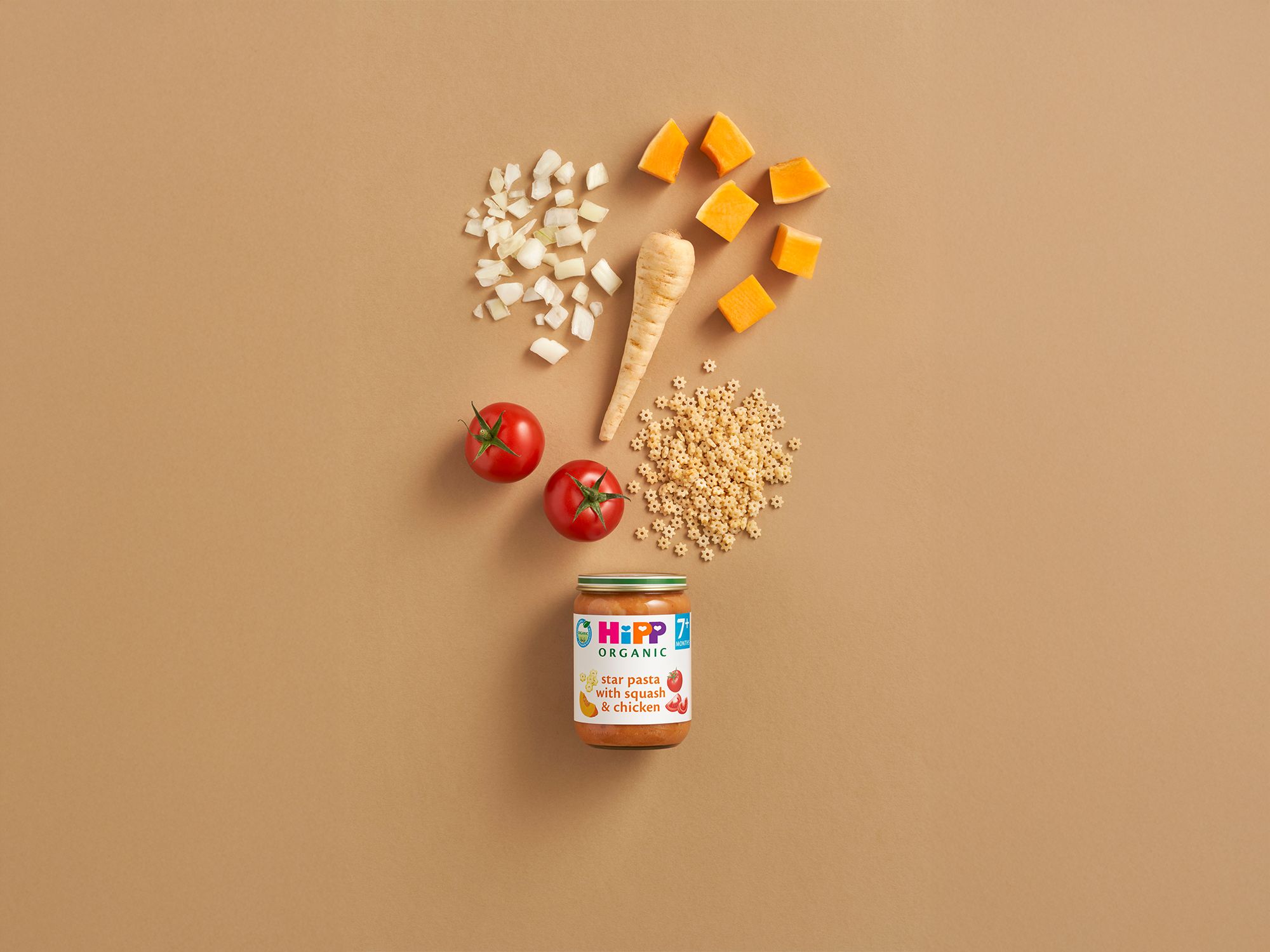 HiPP Organic Star pasta with Squash & Chicken jar surrounded by tomatoes, squash, parsnip and star-shaped pasta on a neutral background
