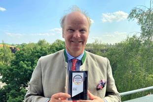 Stefan Hipp hält im Freien den Deutschen Award für Nachhaltigkeitsprojekte vor grüner Landschaft in den Händen.
