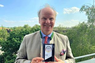 Stefan Hipp hält im Freien den Deutschen Award für Nachhaltigkeitsprojekte vor grüner Landschaft in den Händen.