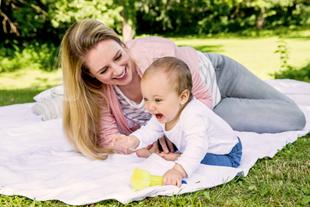 Ein freudiger Moment zwischen einer Frau und einem Baby, die beide auf einer weißen Decke im Freien liegen.