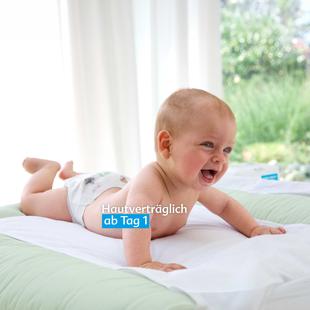 Lachendes Baby liegt auf dem Bauch auf einer Wickelunterlage vor einem Fenster mit Blick ins Grüne