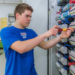 Auszubildender Elektroniker bei HiPP arbeitet konzentriert an einem geöffneten Schaltschrank mit vielen Kabeln und Bauteilen.