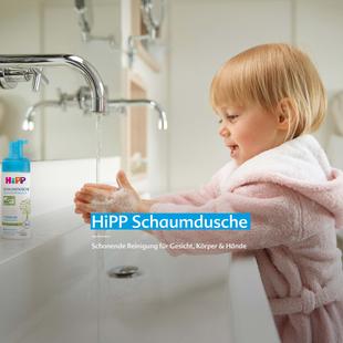 Kleines Kind im rosa Bademantel wäscht lachend die Hände mit HiPP Schaumdusche am Waschbecken mit fließendem Wasser.