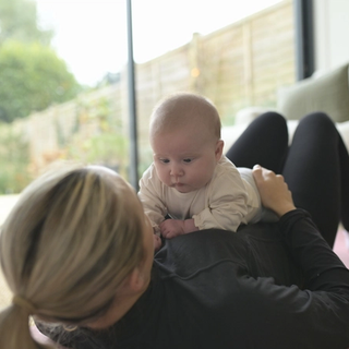 Mum lying on her back on yoga mat with baby on her belly