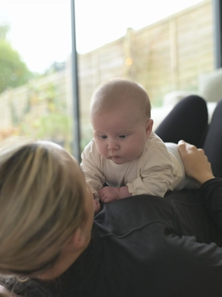 Mum lying on her back on yoga mat with baby on her belly