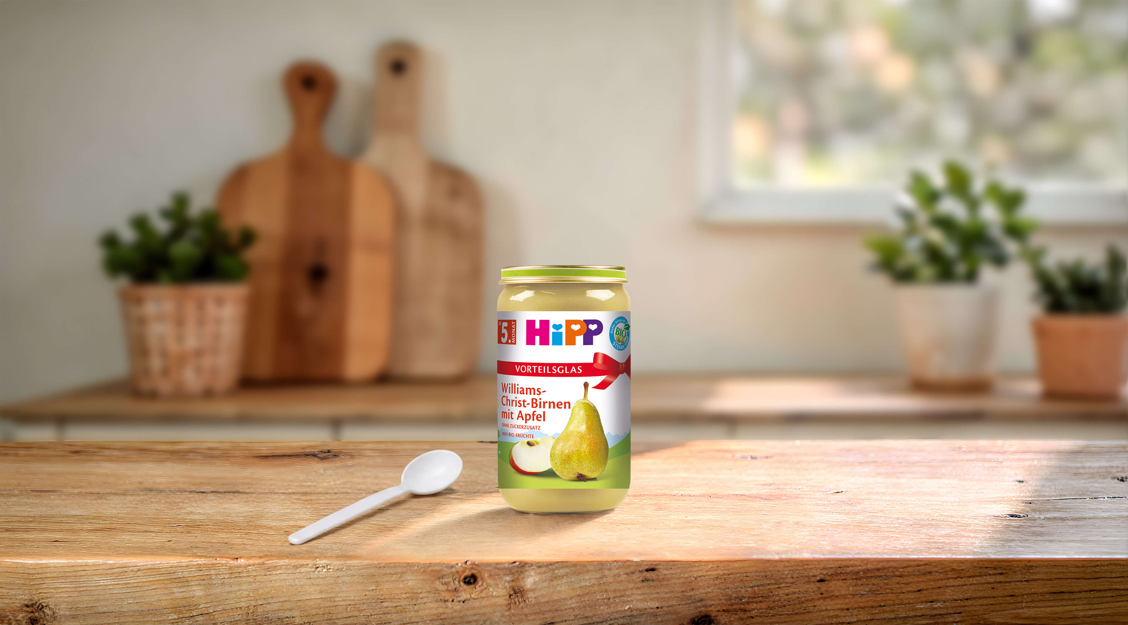 HiPP Bio Vorteils-Glas Williams-Christ-Birnen mit Apfel auf Holztisch in heller, gemütlicher Küche mit Löffel im Vordergrund