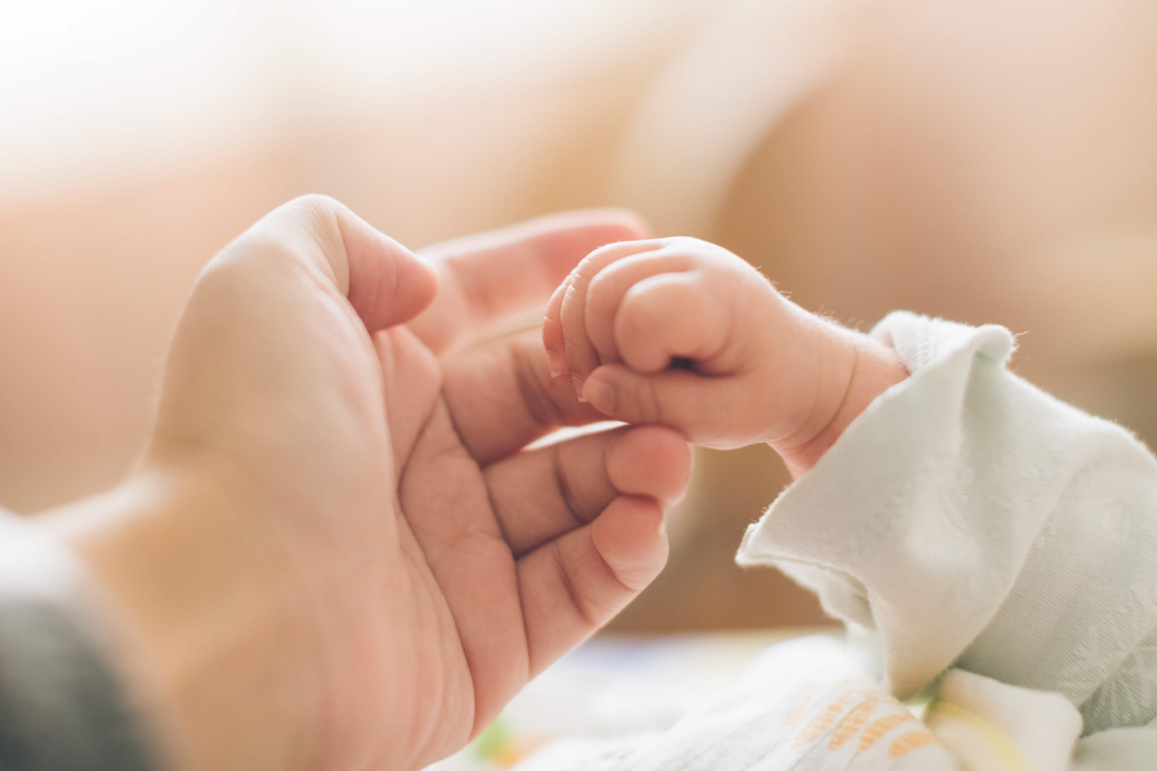 Ein zärtlicher Moment zwischen einem Erwachsenen und einem Baby, in dem die winzige Hand des Babys den Finger des Erwachsenen ergreift und so ein Band des Vertrauens und der Verbundenheit symbolisiert.
