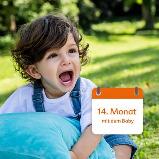 Ein kleines Kind, das in spielerischer Stimmung zu sein scheint, hält ein blaues Kissen in einer Außenumgebung.