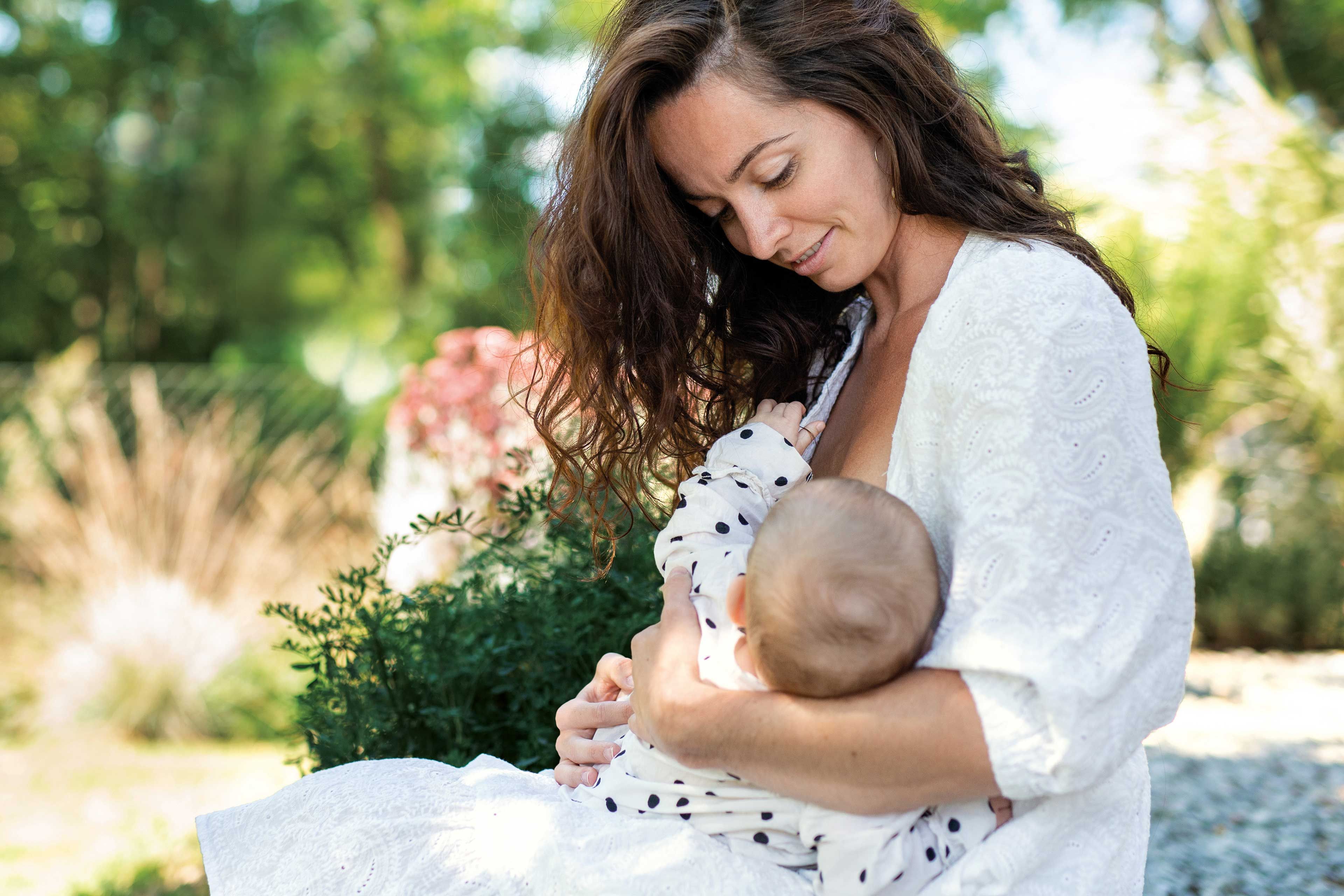 Mama stillt ihr Baby liebevoll im Grünen und genießt einen ruhigen Moment inniger Nähe.