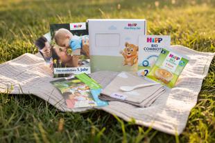 HiPP Baby Club Produktpaket mit Broschüren, Produktproben, Babytuch, Löffel und Coupons auf einer Decke im Gras