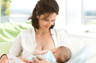 Mutter stillt ihr Baby entspannt auf dem Sofa und hält es nah am Körper, beide wirken ruhig und geborgen.