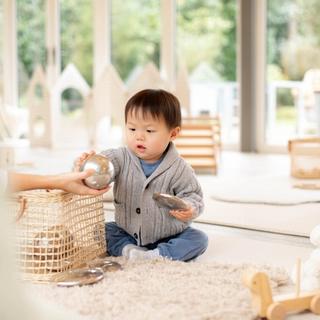 toddler playing with toys on the floor wearing a grey jumper and blue pants.