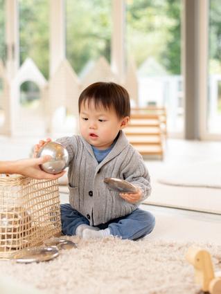 toddler playing with toys on the floor wearing a grey jumper and blue pants.