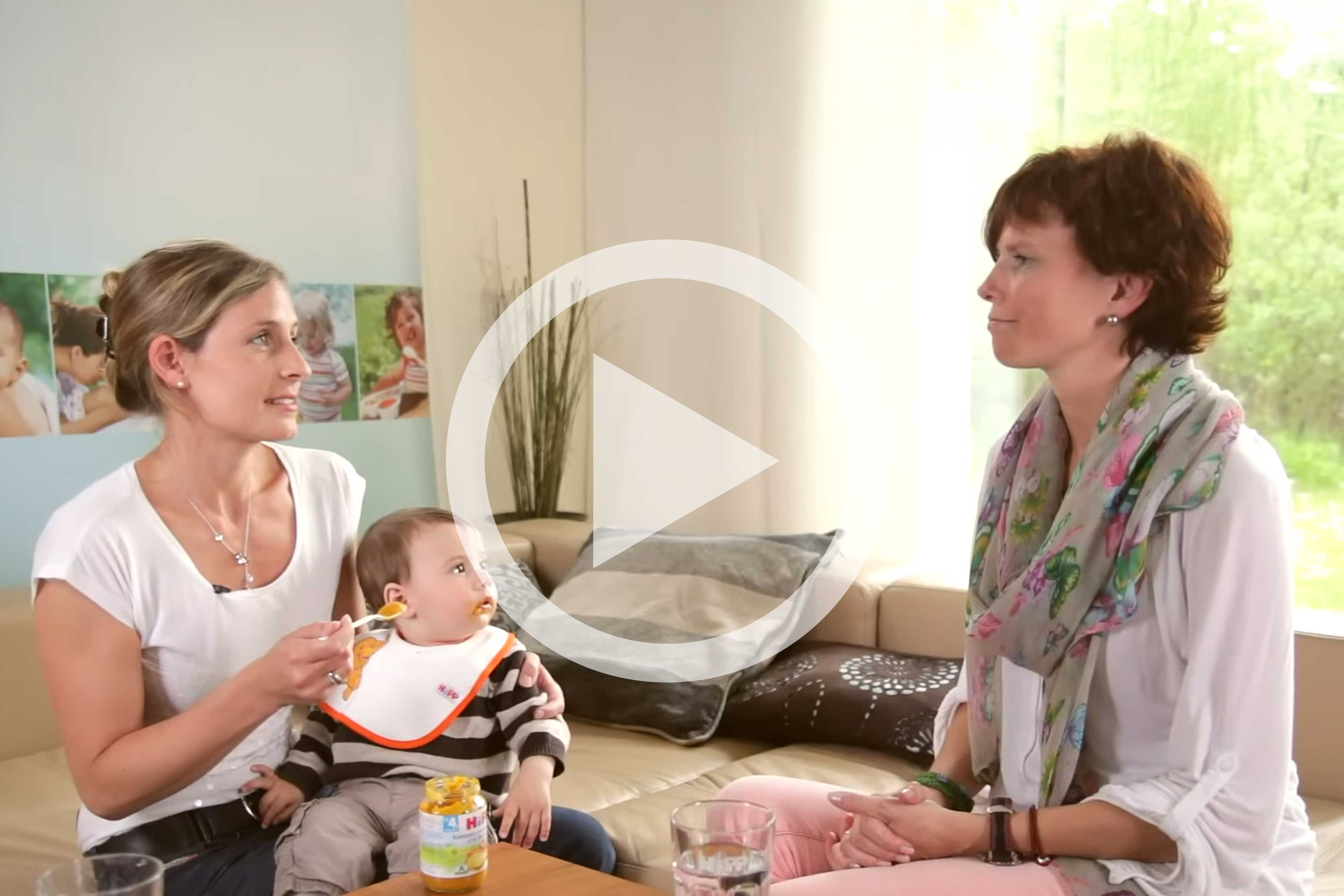 Zwei Frauen im Umgang mit einem Baby, wobei eine Frau das Baby hält und die andere es beobachtet.