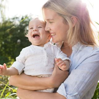 Ein zärtlicher Moment zwischen einer Frau und einem Baby, wobei die Frau lächelt und das Baby freudig lacht.