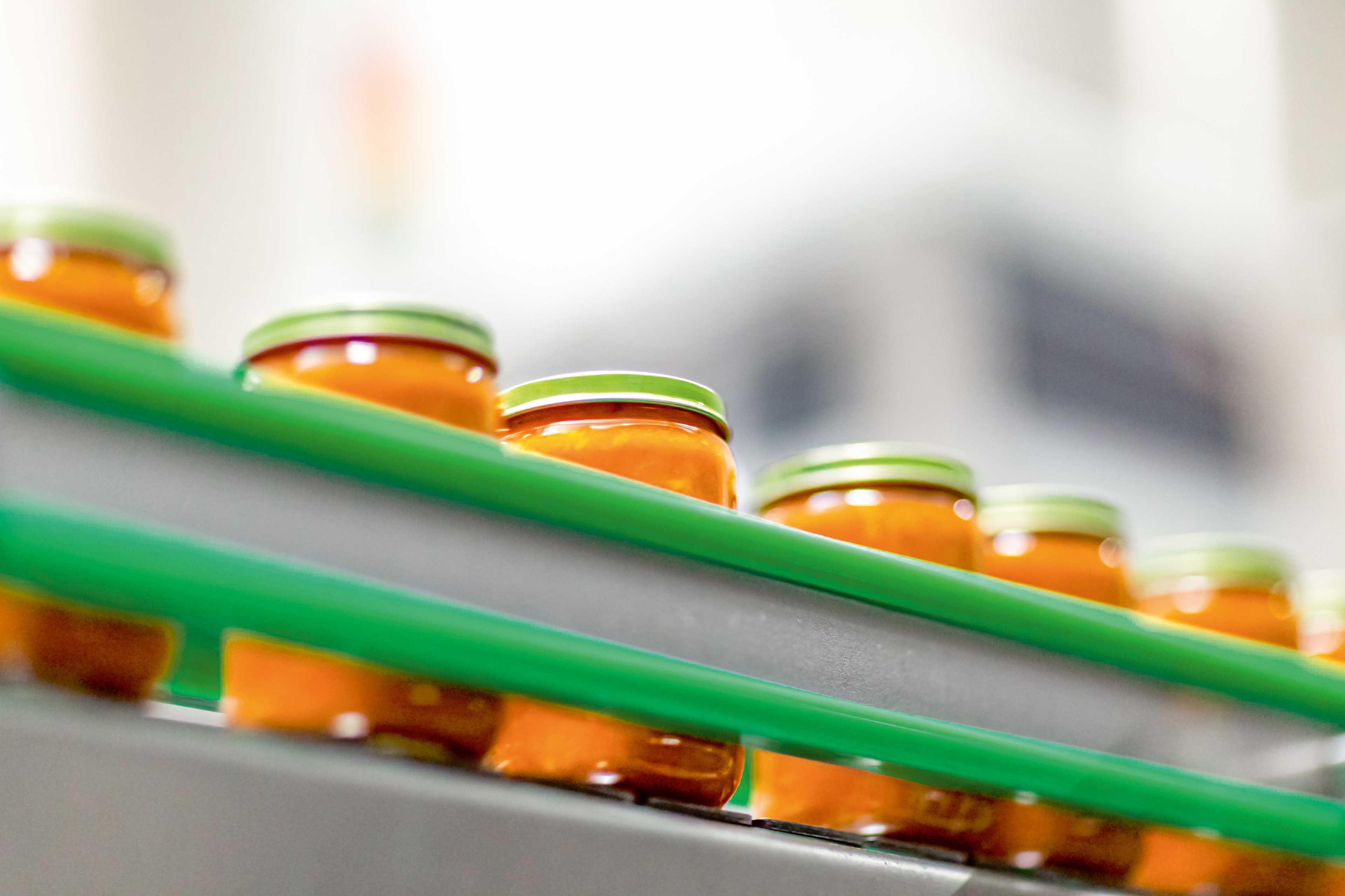 Reihe von Gläsern mit orangefarbener Füllung auf einem Förderband in einer Produktionsanlage