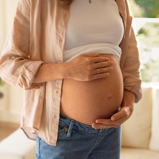 Eine Person, die vermutlich schwanger ist, berührt sanft ihren Bauch.