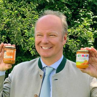 Stefan HiPP lacht in Kamera und hält 2 Babygläschen hoch