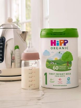 HiPP Organic First Infant Milk tin on a bright kitchen worktop beside a baby bottle, dummy and toy