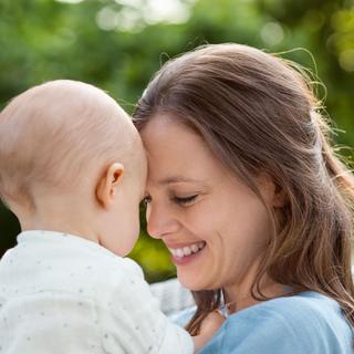 Mutter und Baby lächeln auf einer Decke im Grünen, symbolisieren Kinderwunsch und Familienglück.