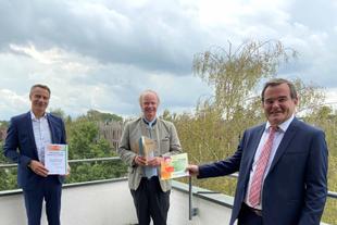 Drei Männer auf einer Terrasse mit Blick ins Grüne, Landrat überreicht HiPP die UN-Dekade-Auszeichnung für biologische Vielfalt.