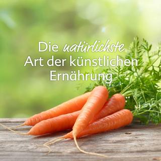 Frische Bundmöhren auf Holztisch vor grünem Hintergrund mit dem Schriftzug „Die natürlichste Art der künstlichen Ernährung“.
