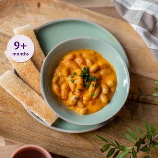 Bowl of homemade baked beans with toast fingers on a wooden board, labelled suitable for babies from 9 months